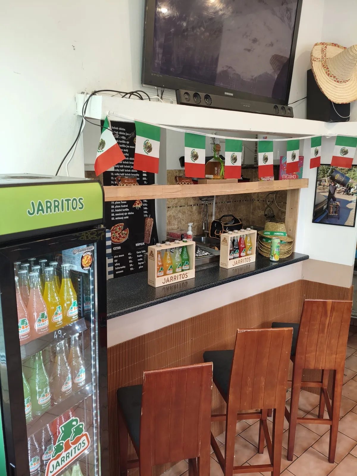 Barový pult s židlemi a lednicí plnou limonád Jarritos